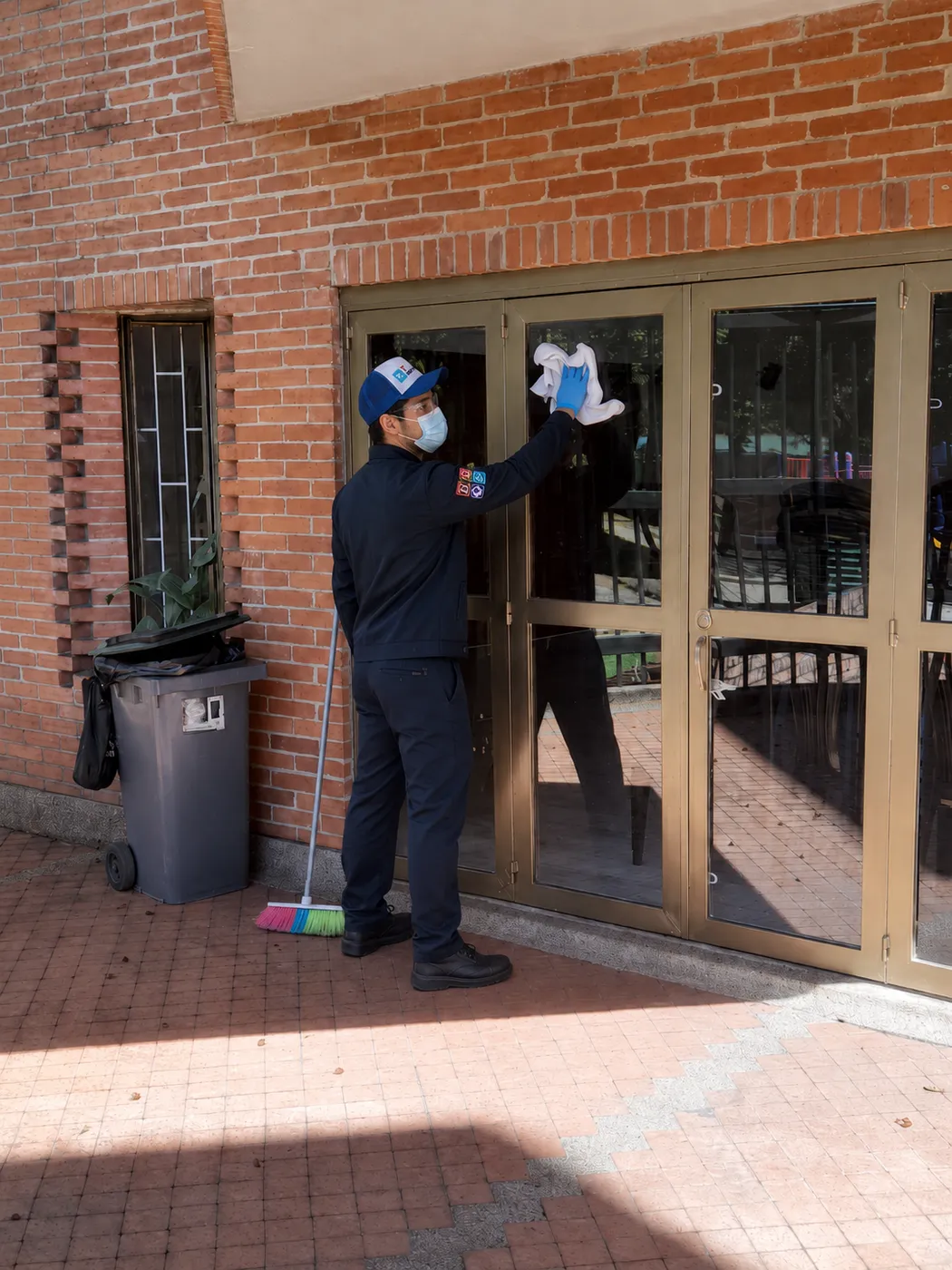 Operario de Te Servimos limpiando los vidrios de una puerta de acceso