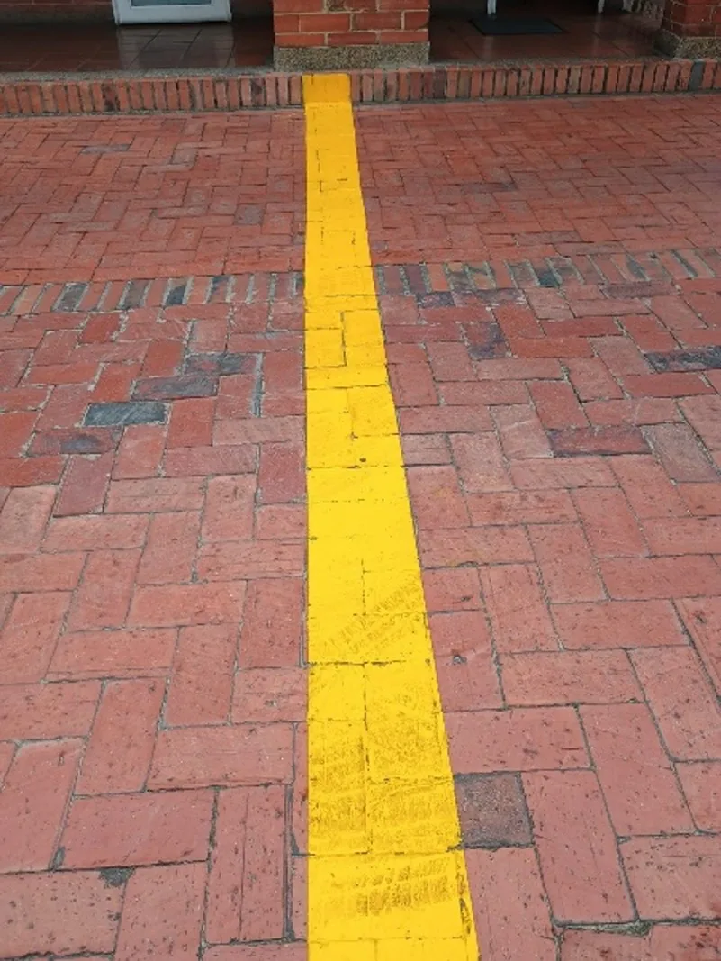 Después — El sendero con la línea guía pintada en amarillo sobre el ladrillo
