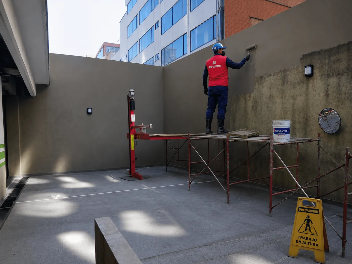 Operario de Te Servimos pintando un muro desde un andamio, con señalización de trabajo en altura