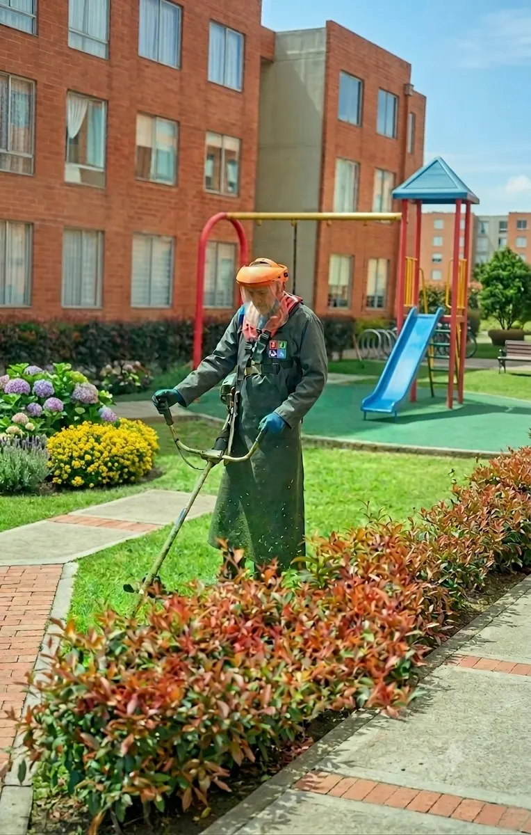 Operario de Te Servimos cortando césped junto al parque infantil de un conjunto